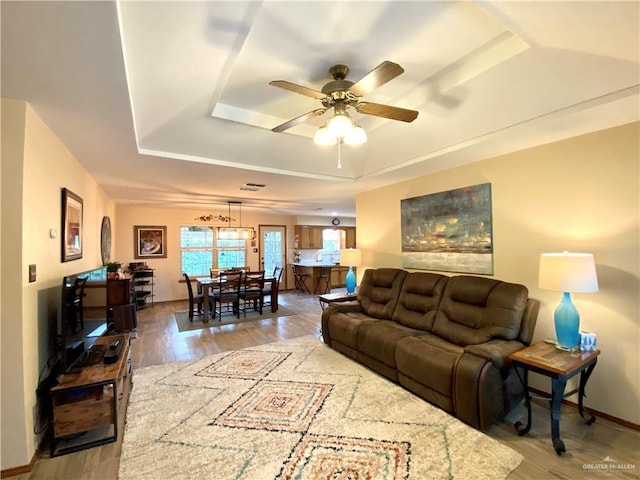 living room with light hardwood / wood-style floors, a raised ceiling, and ceiling fan