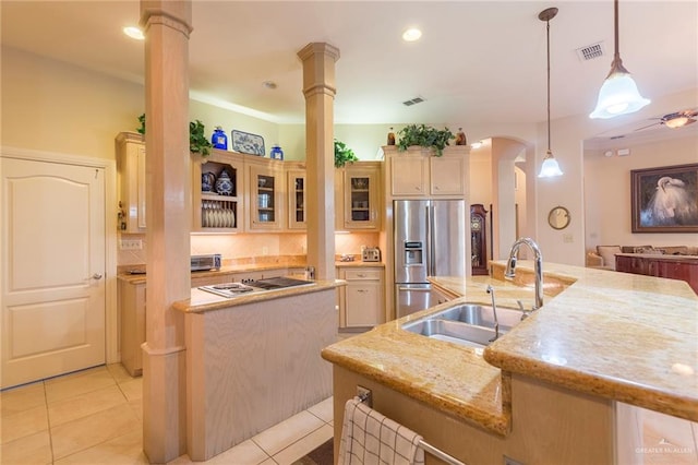 kitchen featuring a kitchen island with sink, sink, stainless steel fridge, decorative light fixtures, and decorative columns