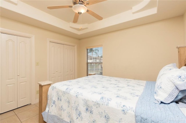 bedroom featuring light tile patterned floors, a tray ceiling, two closets, and ceiling fan