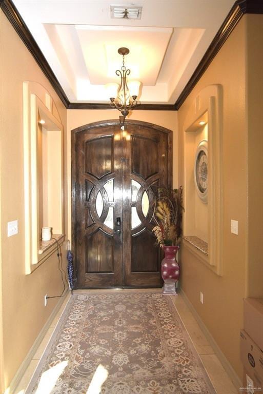 tiled entryway with a tray ceiling, visible vents, an inviting chandelier, and ornamental molding