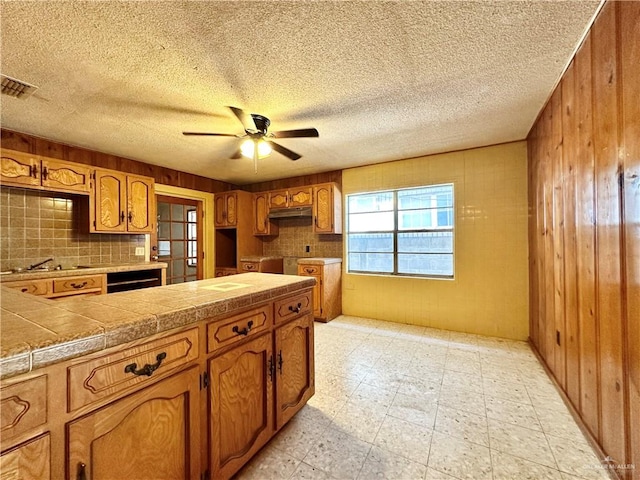 kitchen featuring tasteful backsplash, wooden walls, ceiling fan, and a textured ceiling