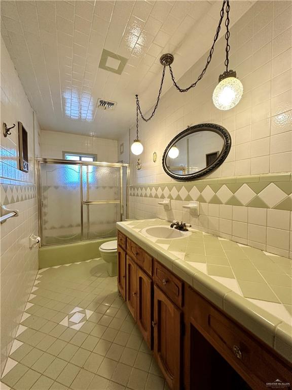 bathroom featuring walk in shower, tile patterned floors, toilet, vanity, and tile walls