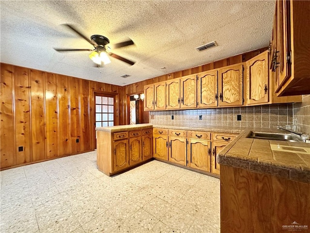 kitchen with wood walls, kitchen peninsula, a textured ceiling, and tasteful backsplash