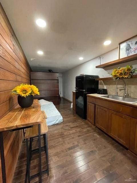 kitchen featuring black refrigerator, dark hardwood / wood-style flooring, wooden walls, and sink