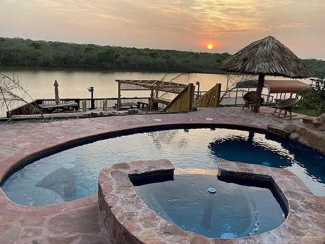 pool at dusk with a patio area, an in ground hot tub, and a water view