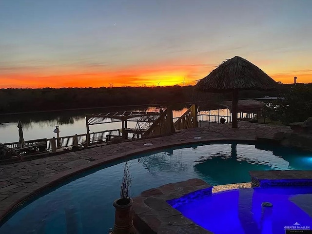 pool at dusk with a gazebo, a patio, and a water view