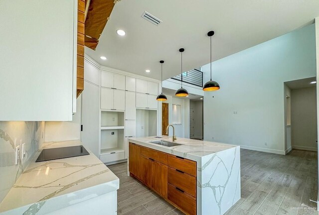 kitchen featuring a large island with sink, sink, white cabinetry, hanging light fixtures, and black electric cooktop