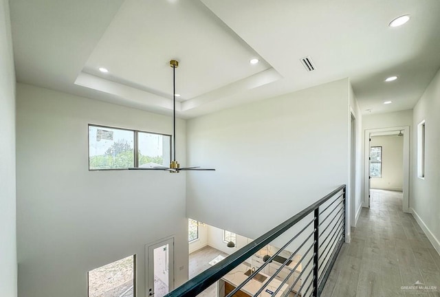 hallway featuring light wood-type flooring and a tray ceiling