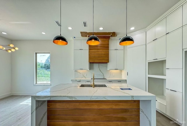 kitchen with hanging light fixtures, white cabinets, an island with sink, and light stone counters