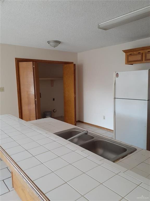 kitchen featuring tile countertops, white refrigerator, sink, and a textured ceiling