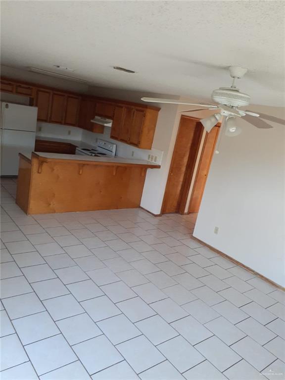 kitchen featuring ceiling fan, kitchen peninsula, white appliances, a breakfast bar, and light tile patterned floors