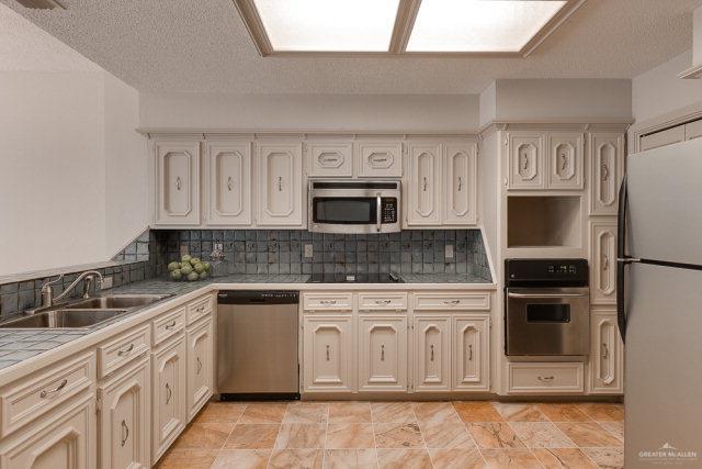 2114 Colorado St, Mission, TX 78572 - kitchen featuring appliances with stainless steel finishes, a sink, tile counters, backsplash, and a textured ceiling