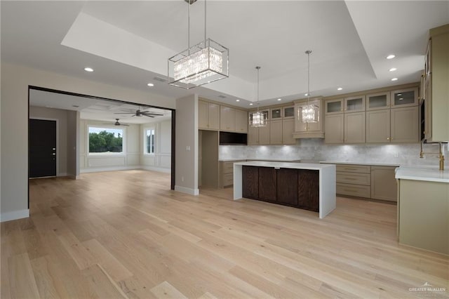 kitchen featuring a tray ceiling, backsplash, recessed lighting, a center island, and light wood finished floors