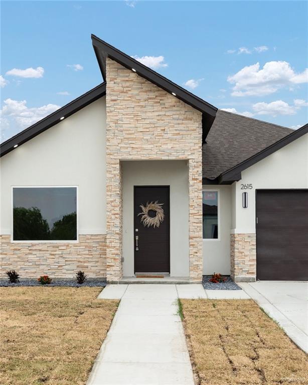 contemporary house with stone siding, stucco siding, an attached garage, a front lawn, and roof with shingles