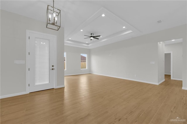 unfurnished living room featuring ceiling fan with notable chandelier, a tray ceiling, and light hardwood / wood-style flooring