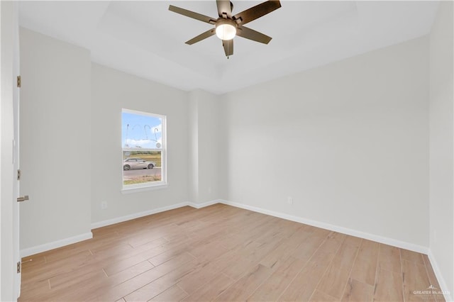 spare room featuring light hardwood / wood-style floors, ceiling fan, and a tray ceiling