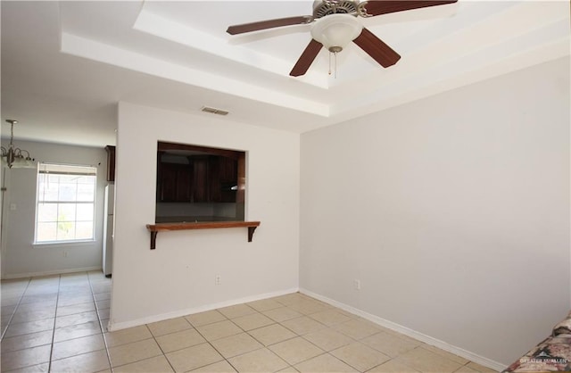 spare room featuring light tile patterned floors, ceiling fan with notable chandelier, and a tray ceiling