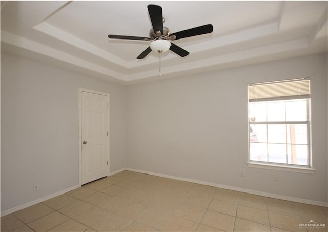 empty room with ceiling fan, light tile patterned flooring, and a raised ceiling