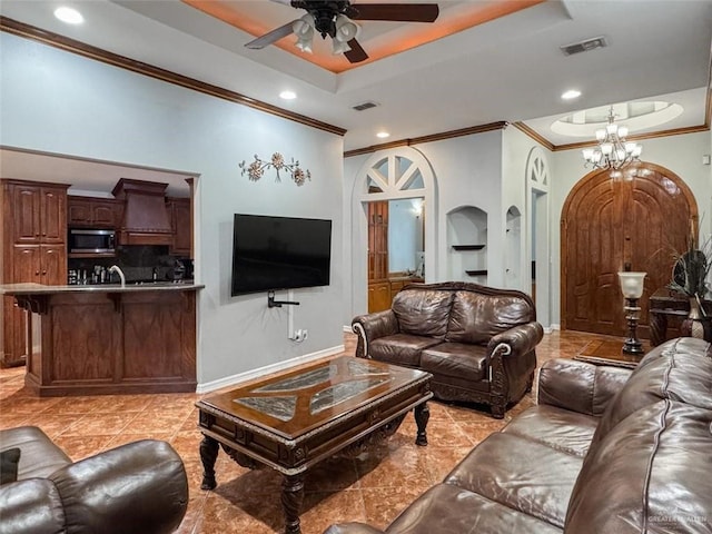 tiled living room with ceiling fan with notable chandelier, ornamental molding, sink, and a tray ceiling