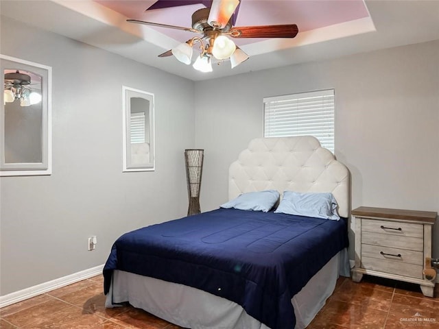 bedroom with a tray ceiling, dark tile patterned flooring, and ceiling fan