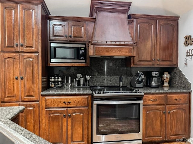 kitchen featuring premium range hood, backsplash, dark stone counters, and stainless steel appliances