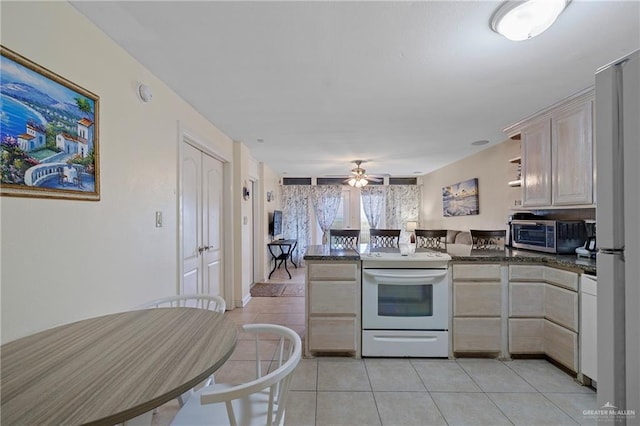 kitchen featuring light tile patterned flooring, ceiling fan, kitchen peninsula, white appliances, and dark stone counters