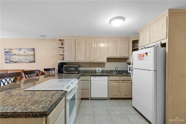 kitchen with white appliances, dark stone counters, sink, and light tile patterned floors