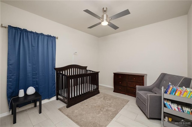 tiled bedroom featuring a nursery area and ceiling fan