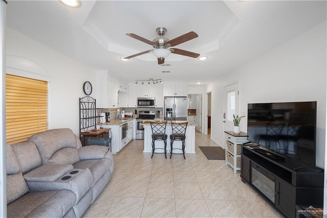 living area with a raised ceiling, ceiling fan, and recessed lighting