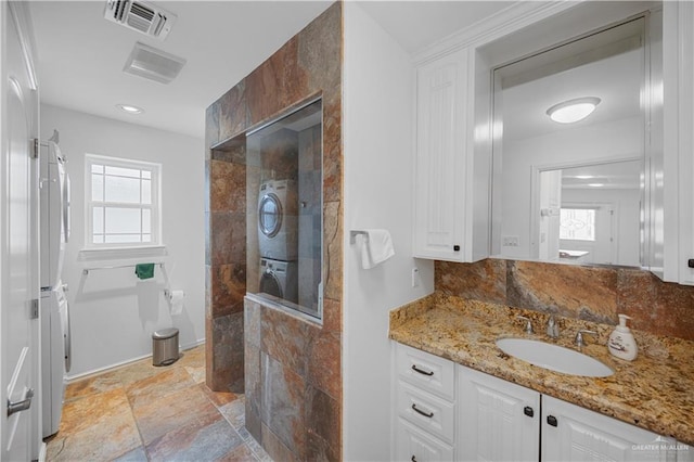 full bathroom with visible vents, decorative backsplash, vanity, stacked washing maching and dryer, and walk in shower