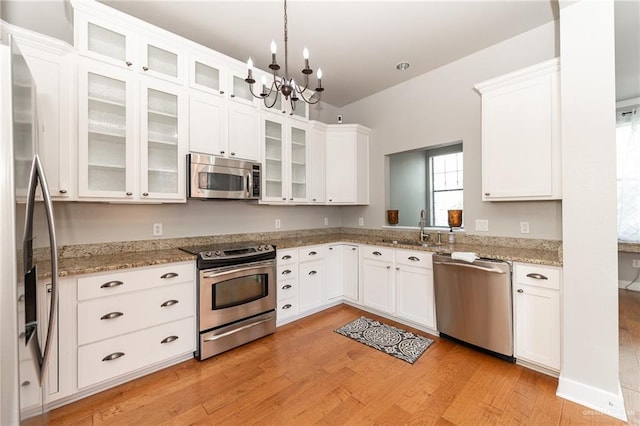 kitchen with appliances with stainless steel finishes, light wood-type flooring, hanging light fixtures, white cabinets, and sink