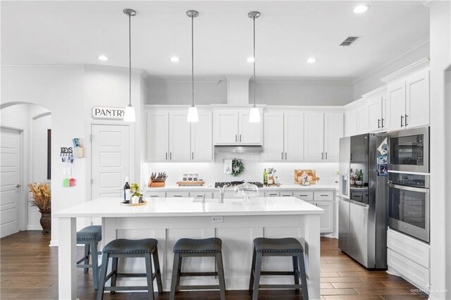 kitchen with decorative light fixtures, stainless steel appliances, a kitchen island with sink, and dark wood-type flooring