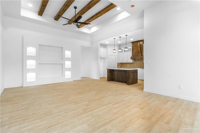 unfurnished living room with beamed ceiling, light wood-style floors, baseboards, and ceiling fan