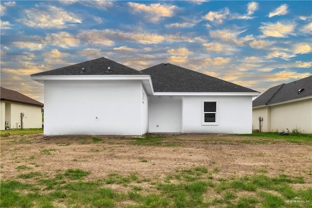 back of house with stucco siding and roof with shingles