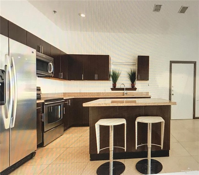 kitchen featuring a breakfast bar, a kitchen island, light tile patterned floors, and appliances with stainless steel finishes