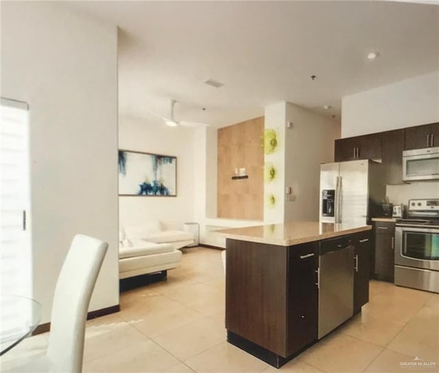 kitchen featuring light tile patterned floors, a center island, stainless steel appliances, and ceiling fan