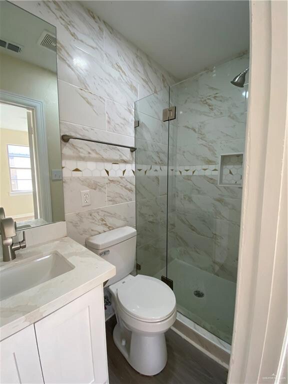 bathroom featuring vanity, toilet, wood-type flooring, and a tile shower