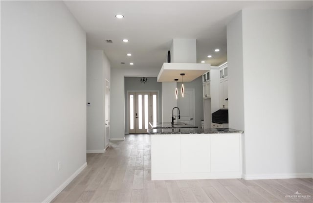 kitchen with kitchen peninsula, light wood-type flooring, decorative light fixtures, dark stone countertops, and white cabinetry