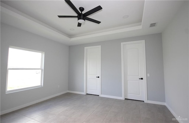 unfurnished bedroom with ceiling fan, light tile patterned floors, and a tray ceiling