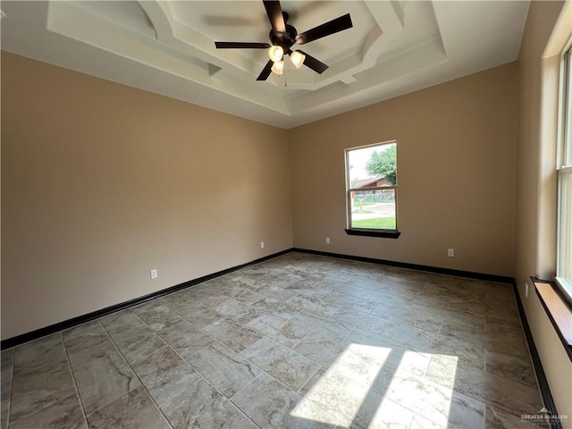 spare room featuring baseboards, a tray ceiling, stone finish floor, and ceiling fan