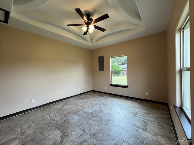 unfurnished room featuring ceiling fan, electric panel, a raised ceiling, baseboards, and stone tile floors