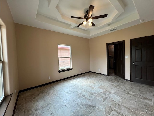 empty room featuring a raised ceiling, stone finish floor, a ceiling fan, baseboards, and visible vents