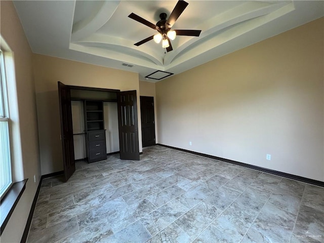 unfurnished bedroom with a raised ceiling, baseboards, stone finish floor, and multiple windows