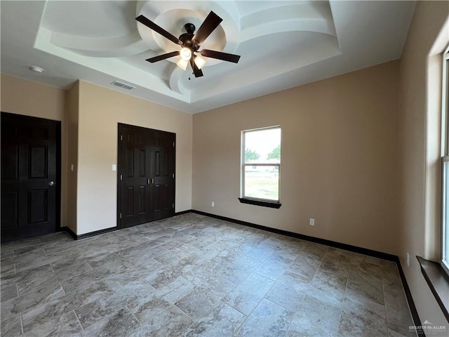 unfurnished bedroom featuring ceiling fan, stone finish flooring, visible vents, baseboards, and a tray ceiling