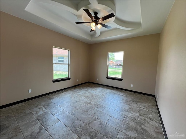 spare room with baseboards, a ceiling fan, a tray ceiling, and a wealth of natural light