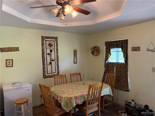 dining room with a raised ceiling, wood-type flooring, and ceiling fan