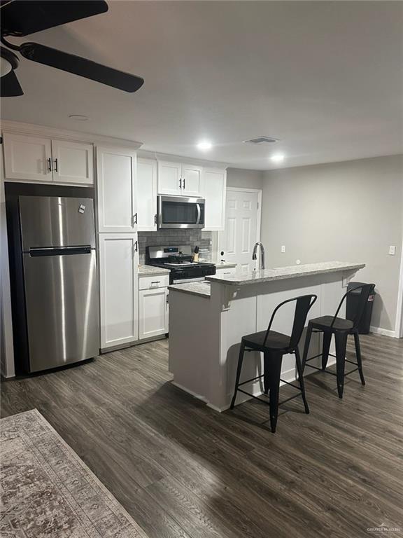 kitchen with a kitchen bar, dark hardwood / wood-style flooring, stainless steel appliances, white cabinets, and an island with sink