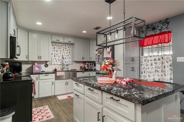 kitchen featuring dark stone countertops, appliances with stainless steel finishes, sink, a center island, and dark hardwood / wood-style floors