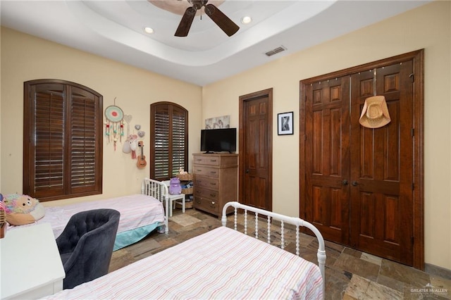 bedroom with ceiling fan, a raised ceiling, and two closets