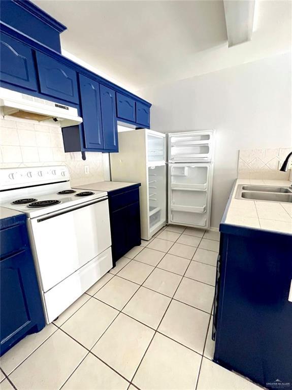 kitchen featuring white electric stove, blue cabinetry, light tile patterned floors, a sink, and under cabinet range hood